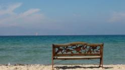 Das Bild zeigt eine Bank aus Holz vor dem Strand und dem Meer. Das Bild steht für Urlaub, Urlaubsgeld und Urlaubsabgeltung 